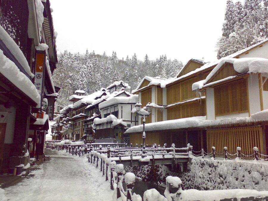 The Ginzan Onsen wooden ryokan street at night, with gas lamps illuminating the snow-covered facades
