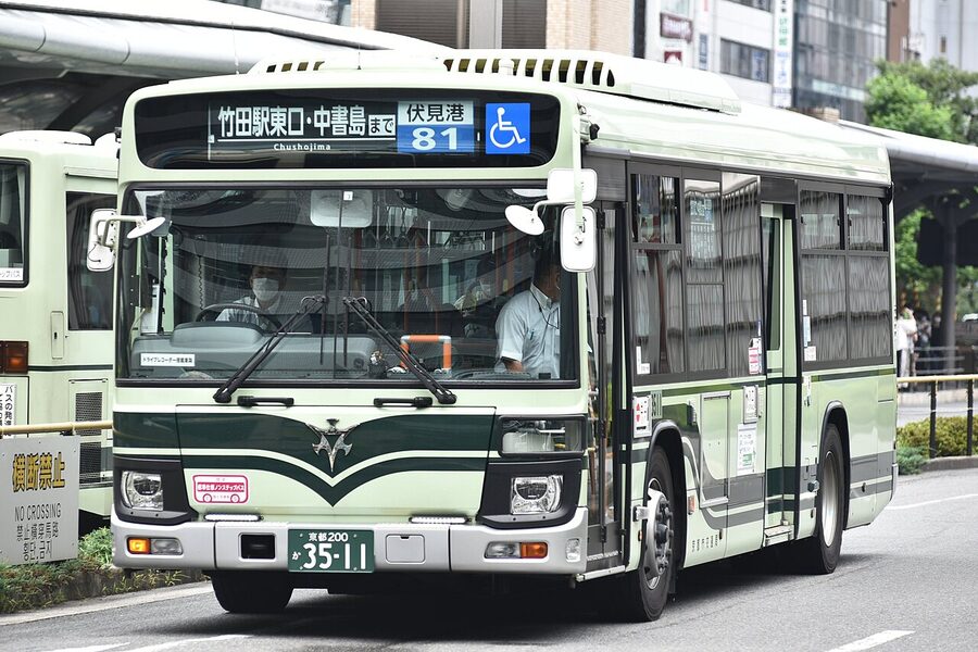 A green-and-cream Kyoto City Bus on a downtown street, the route number visible in the front window