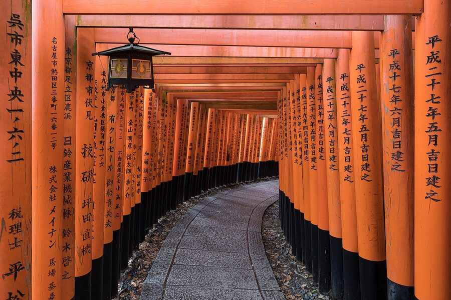 Bright orange torii gates lined up along a stone path at Fushimi Inari Taisha, with a stone lantern visible at the top