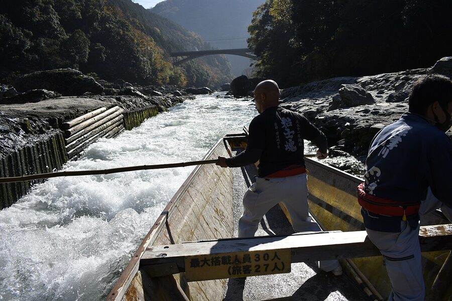 A wooden riverboat on the Hozugawa river with a small group of passengers, surrounded by wooded gorge cliffs