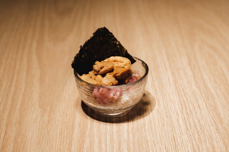 A small glass bowl on a wooden surface holding a delicately arranged seafood course, lit naturally