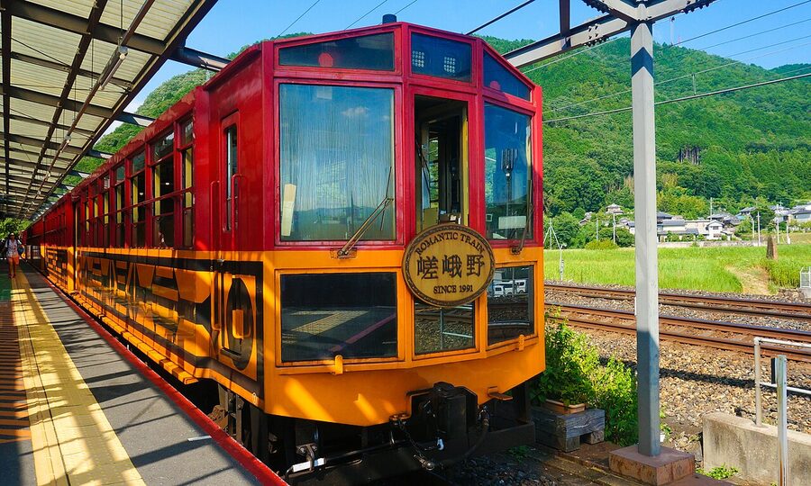 A Sagano Romantic Train carriage with open windows on a track running along a wooded gorge
