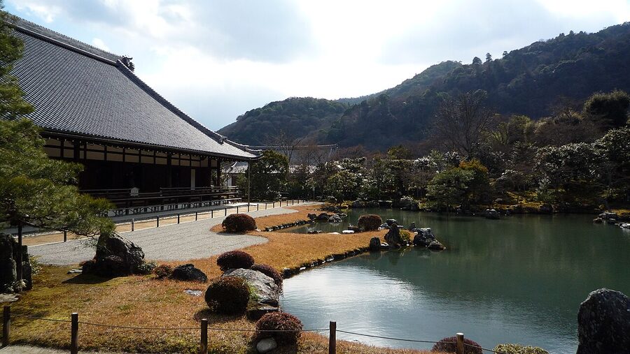 Tenryu-ji's pond garden in autumn, with red maple foliage reflected on still water and Mt Arashiyama in the background