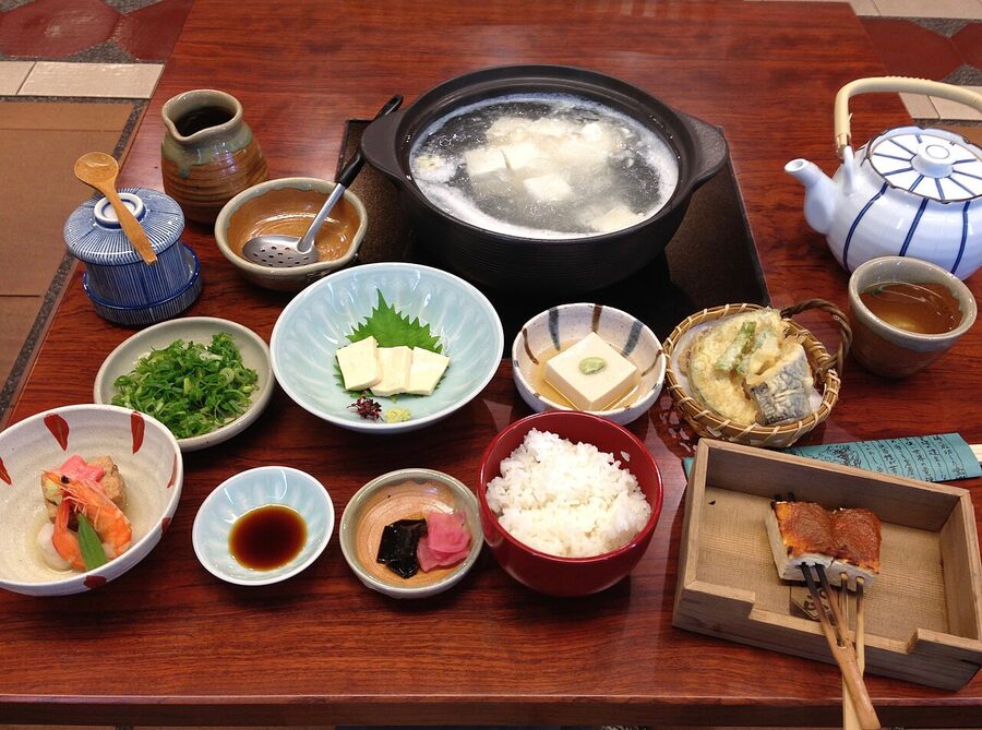 A traditional Kyoto yudofu meal set with a clay pot of boiled tofu and several side dishes on a black tray
