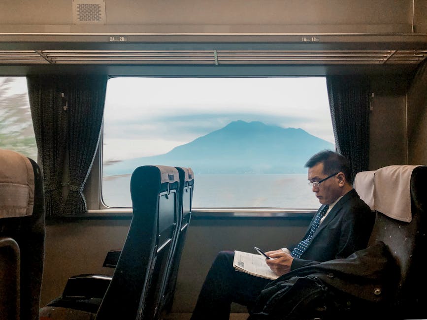 Mount Fuji visible through a passenger train window with a man reading in the foreground