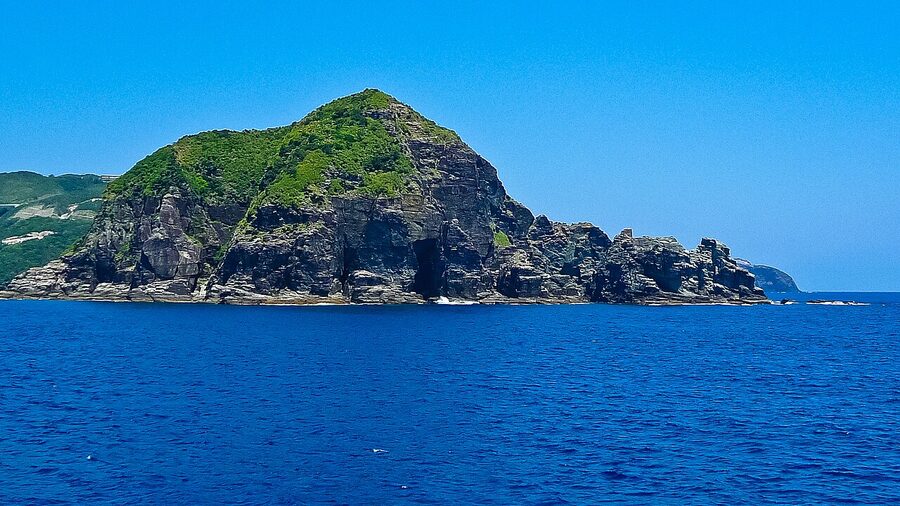 A small ferry approaching one of the Kerama Islands, white sand and coral seabed visible through clear water
