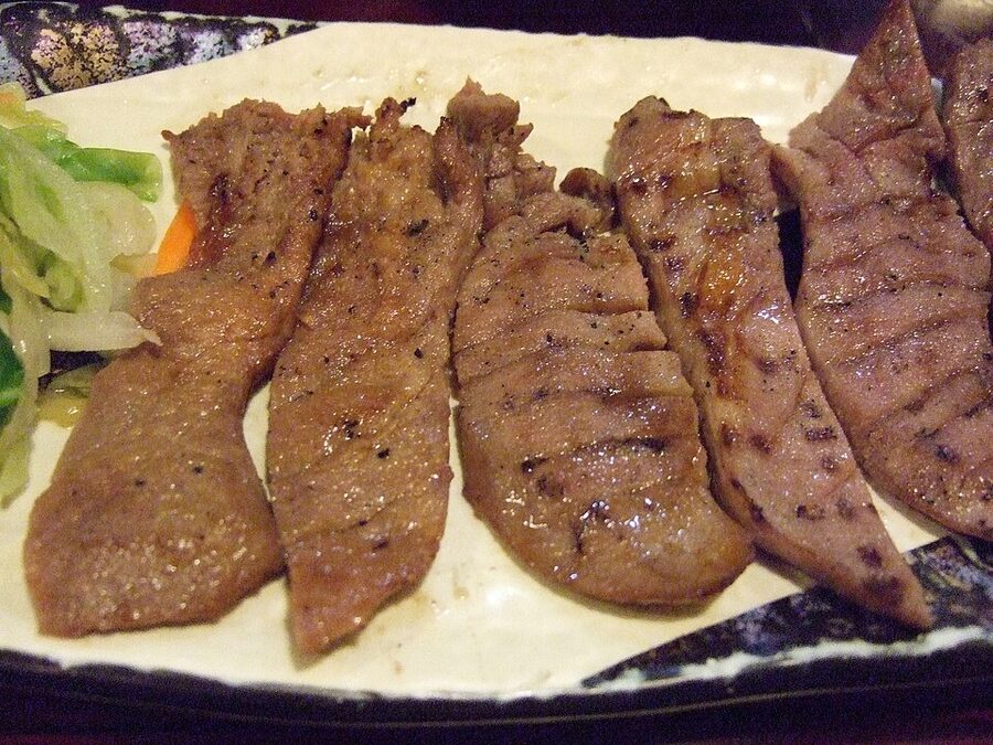 Charcoal-grilled gyutan beef tongue slices on a black plate