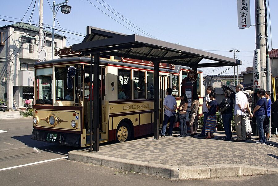 Sendai Loople sightseeing bus stopped at a downtown bus shelter on a sunny day