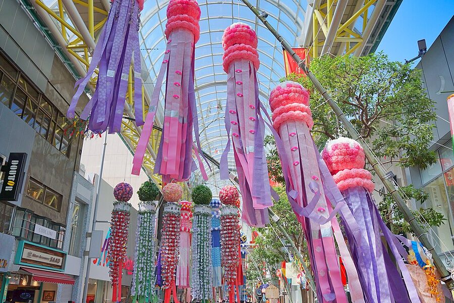 Crowds walking under tall colourful Sendai Tanabata festival streamers in an arcade