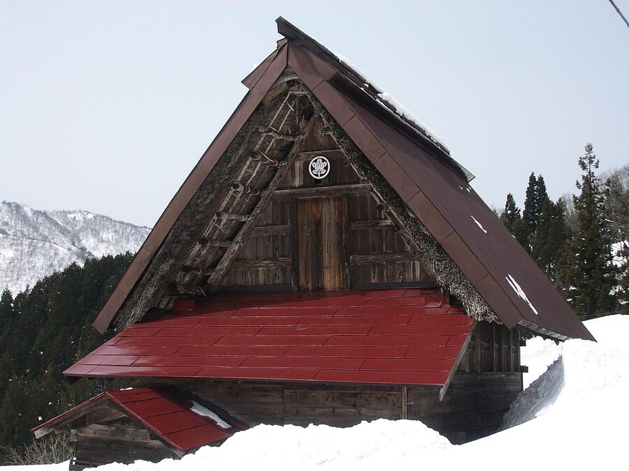 Gassho-zukuri farmhouse with corrugated tin sheeting partly covering the thatch, showing repair material