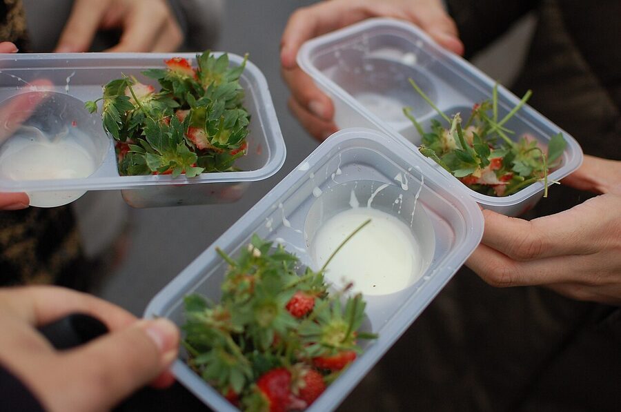 Hands holding fresh-picked strawberries with a small condensed milk container