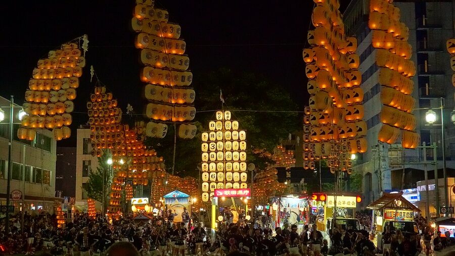 Performer balancing tall illuminated bamboo pole with paper lanterns at Akita Kanto Festival