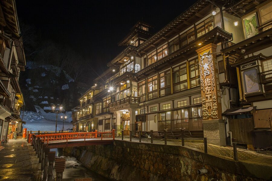 Ginzan Onsen wooden ryokan and bridge at night with snow, Yamagata